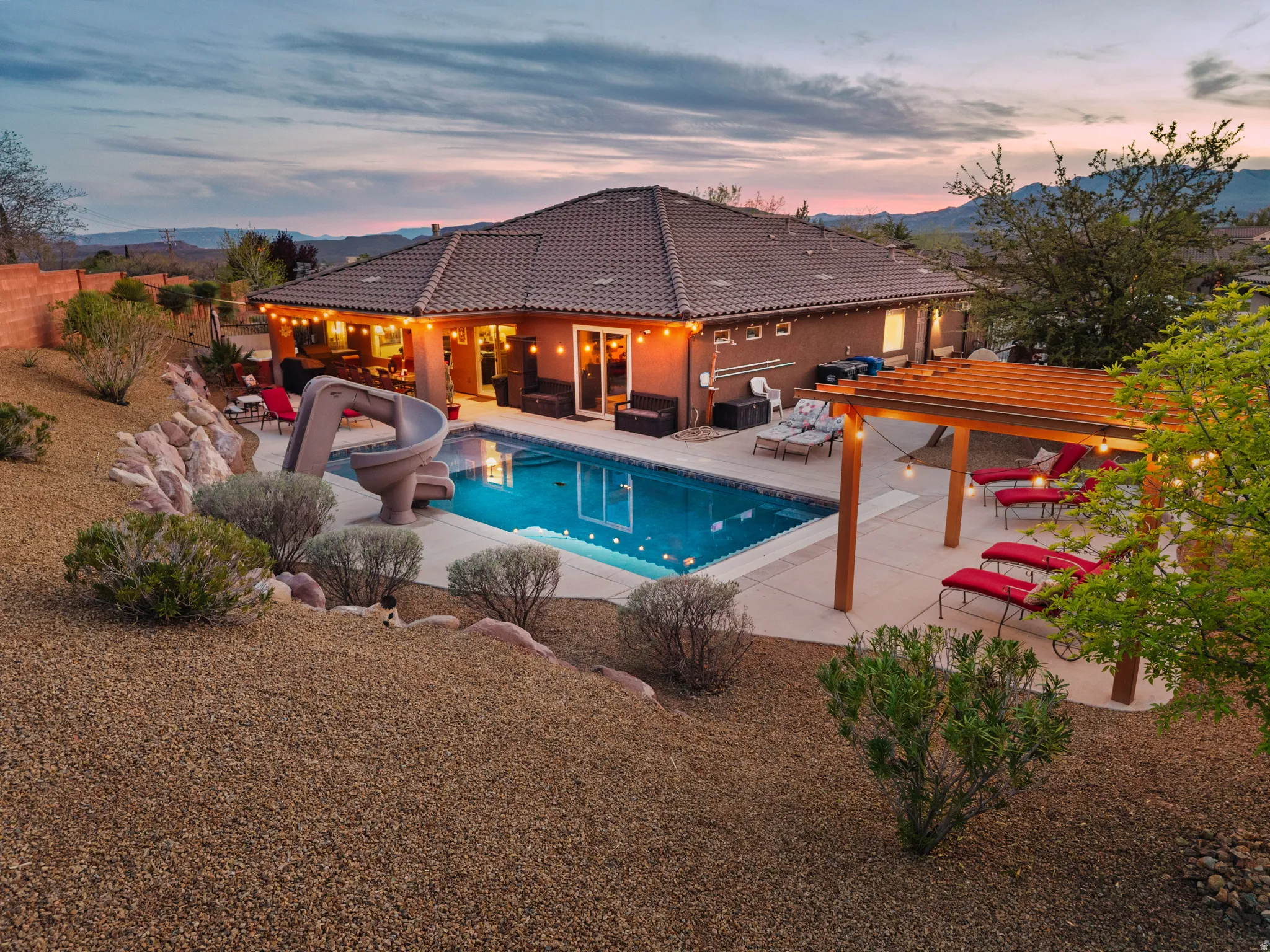 Pool at dusk featuring outdoor seating, a patio, a water slide, and a fenced backyard