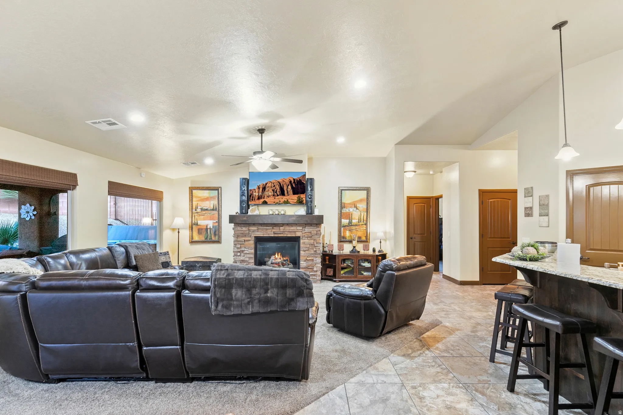Living area with lofted ceiling, a ceiling fan, and a stone fireplace