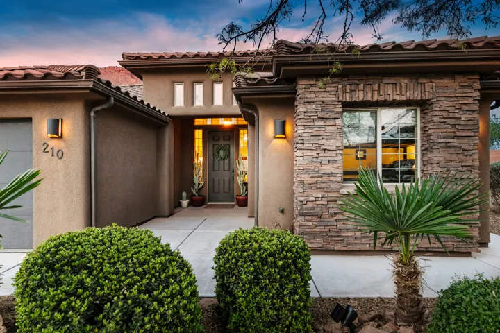 Exterior entry at dusk featuring stone siding, stucco siding, a garage, and a tiled roof