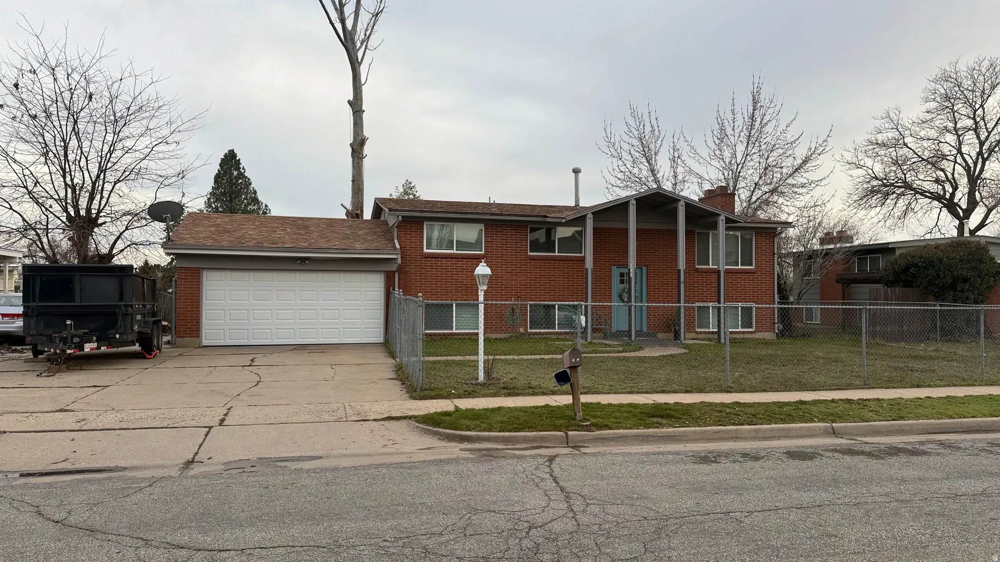 Split foyer home featuring a garage, brick siding, driveway, a fenced front yard, and a chimney