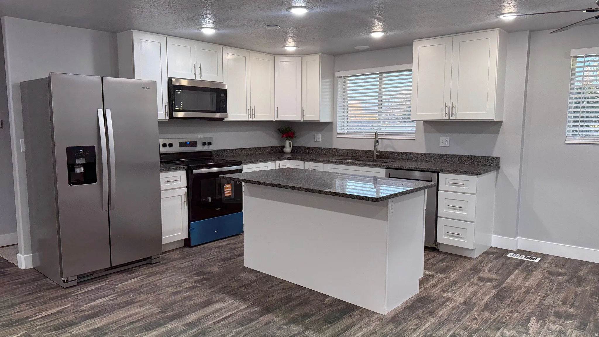 Kitchen with stainless steel appliances, dark stone countertops, white cabinetry, a textured ceiling, and a kitchen island
