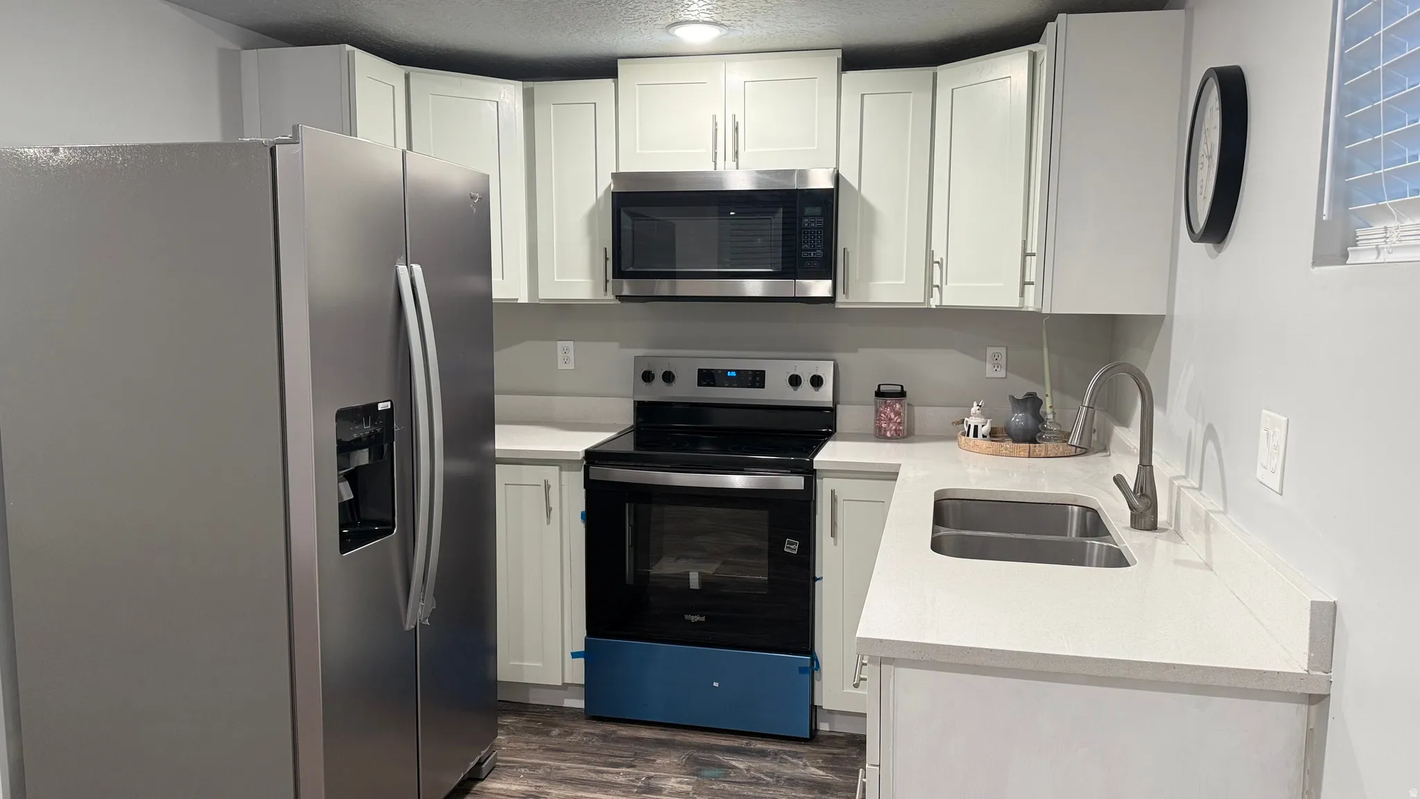 Kitchen with stainless steel appliances, light stone counters, white cabinetry, dark wood-style floors, and a textured ceiling