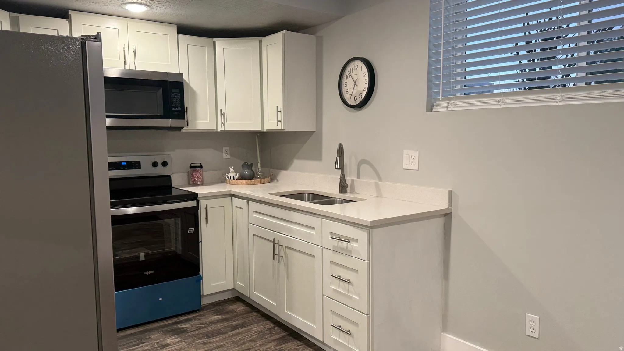 Kitchen featuring stainless steel appliances, white cabinets, light stone counters, and dark wood-style flooring