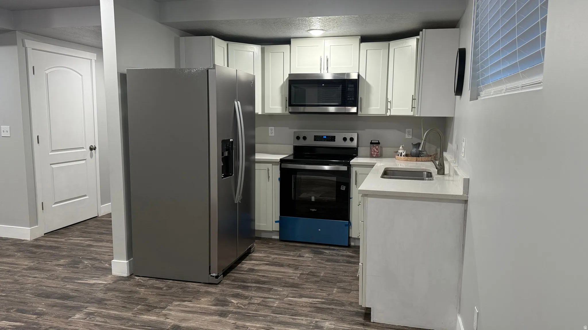 Kitchen with stainless steel appliances, dark wood finished floors, and white cabinetry