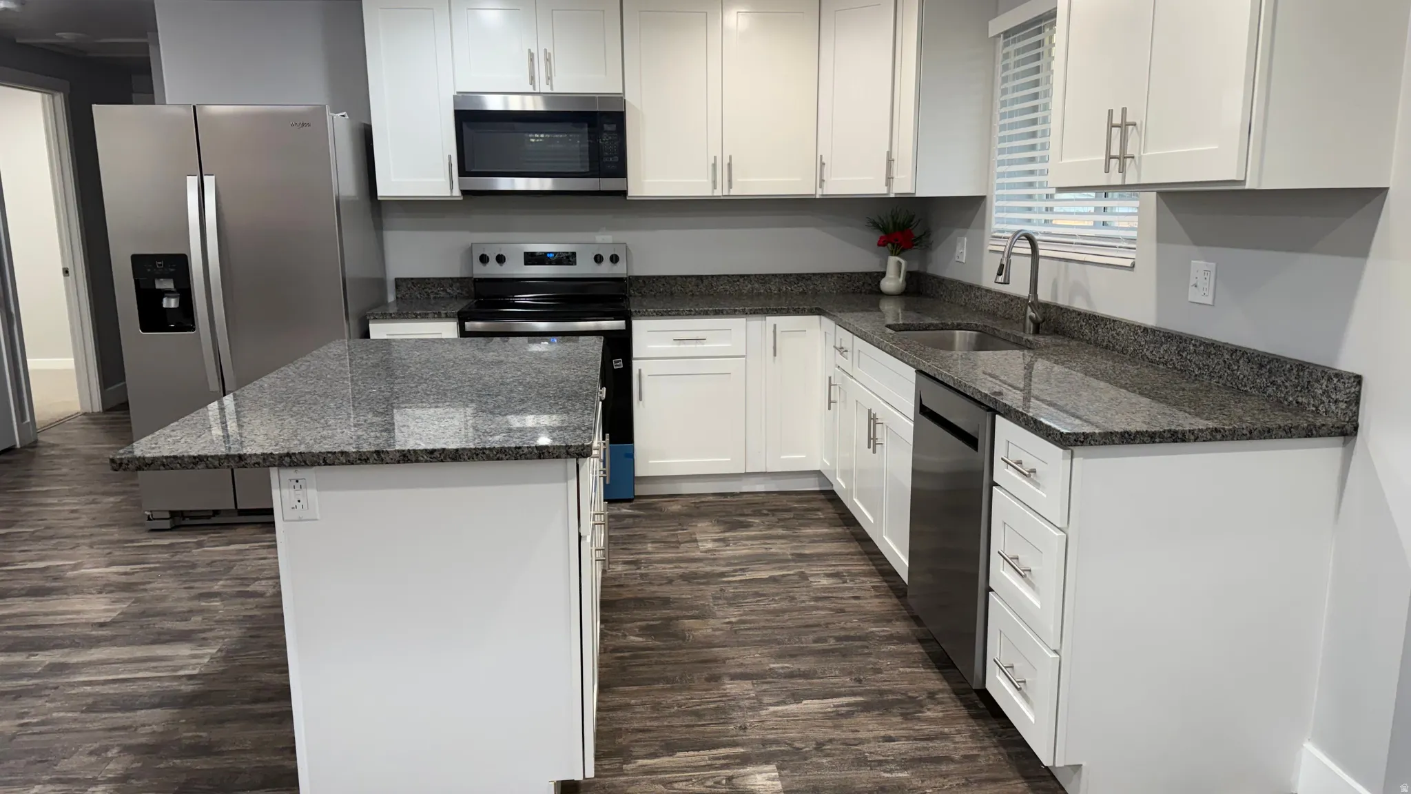 Kitchen with dark stone counters, stainless steel appliances, a center island, dark wood-type flooring, and white cabinetry