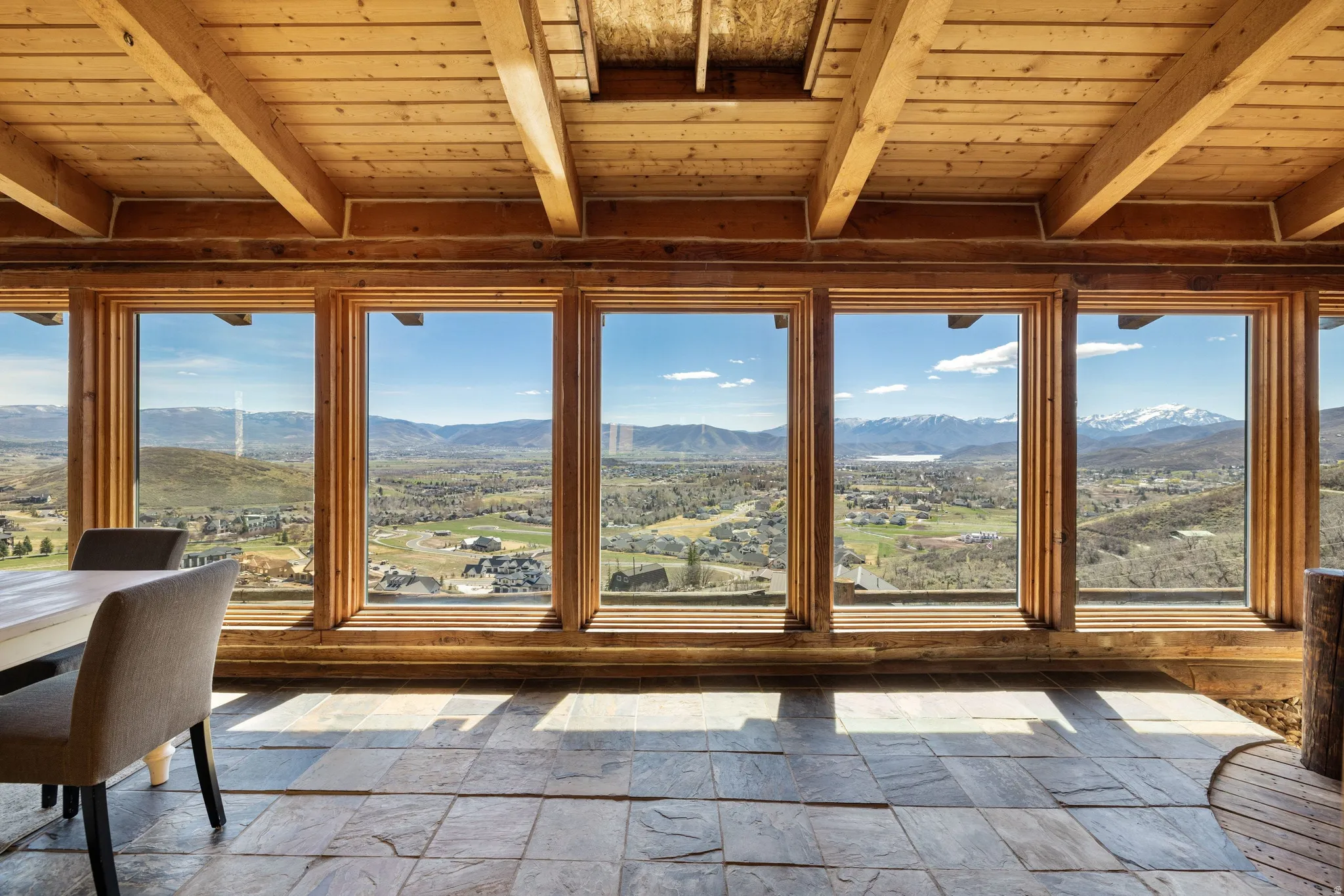 Sunroom / solarium with stone tile floors, a mountain view, and a wood ceiling with exposed beams