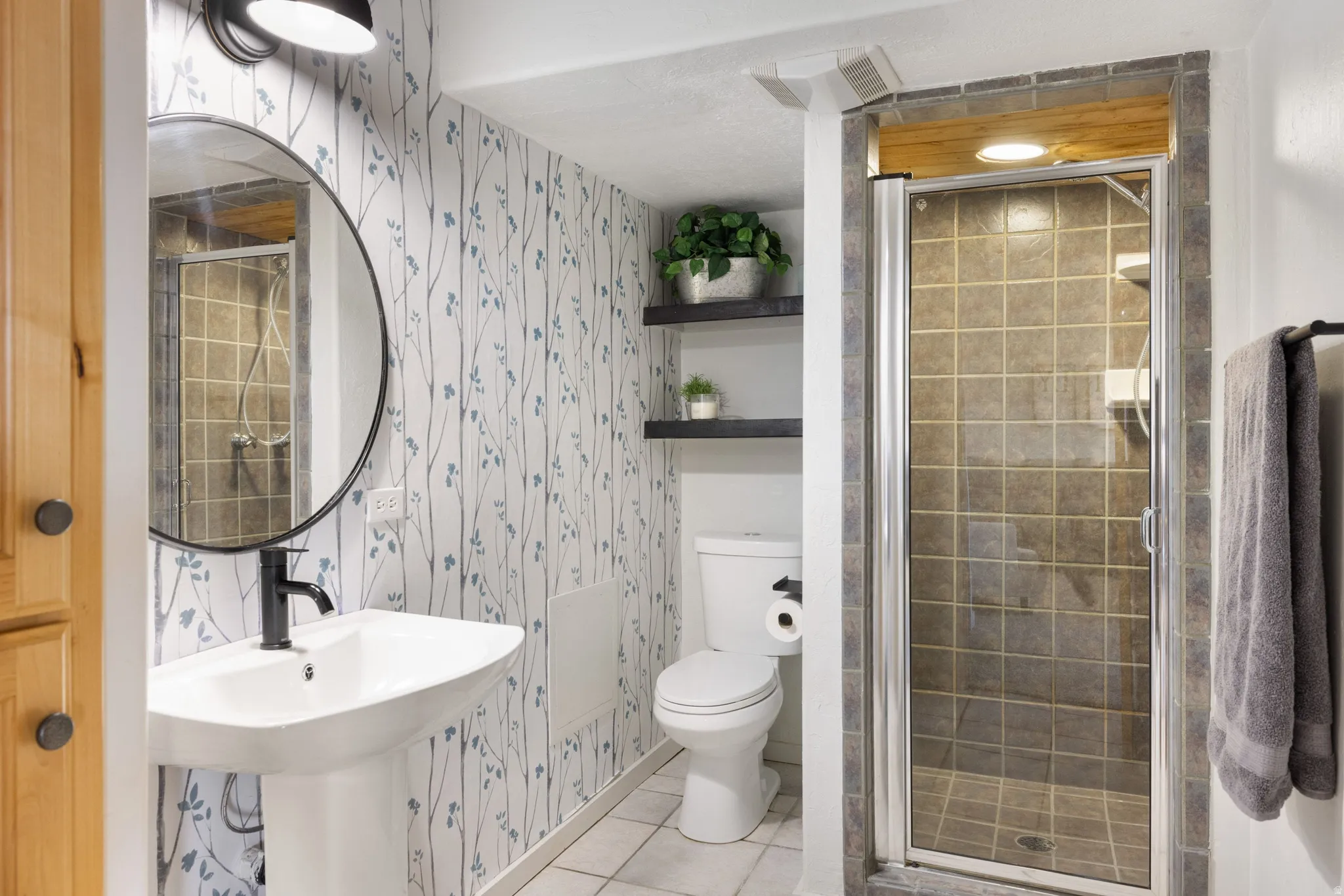 Full bathroom with wallpapered walls, a shower stall, and light tile patterned floors