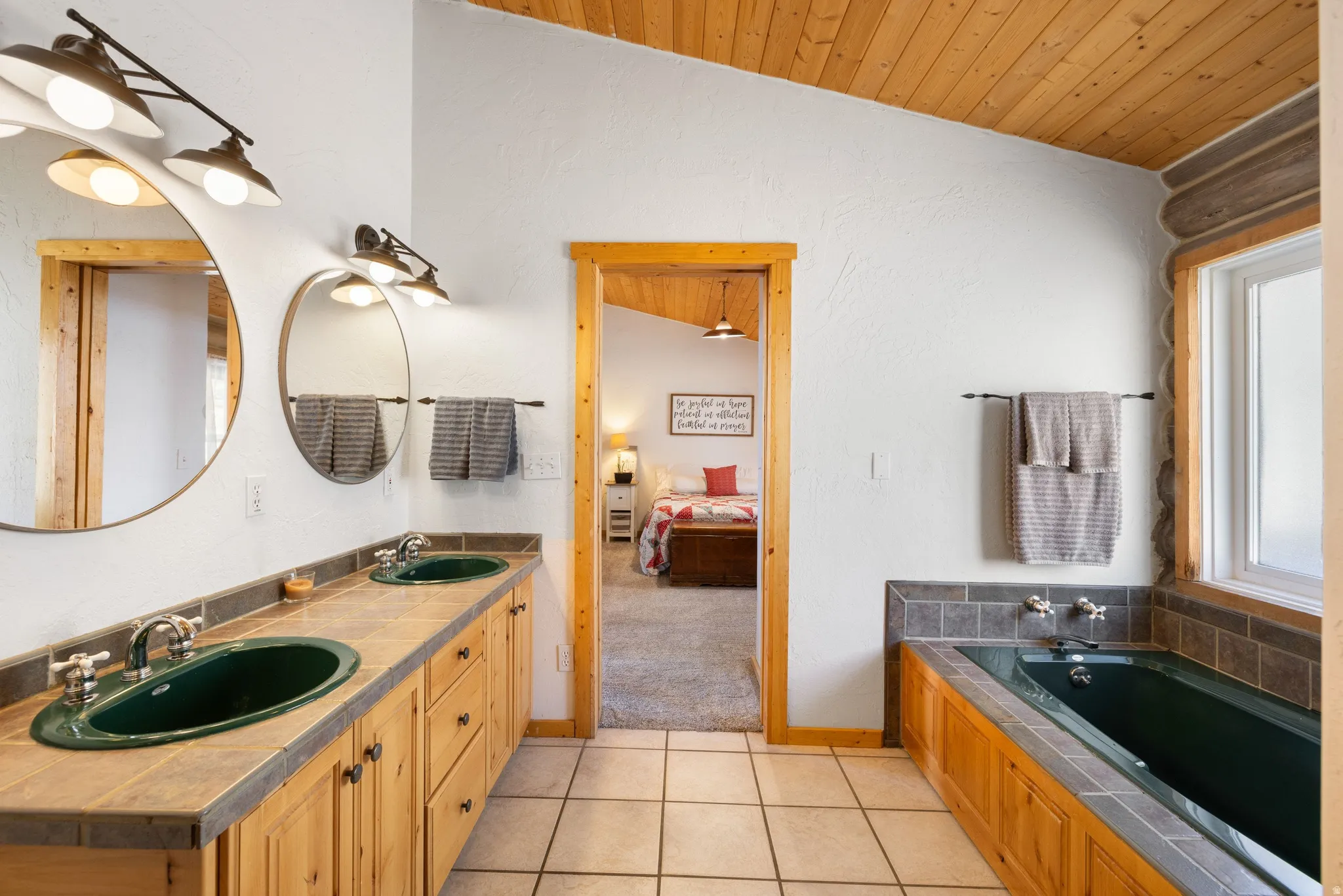 Bathroom featuring ensuite bath, a vaulted wooden ceiling, double vanity, a bath, and light tile patterned floors