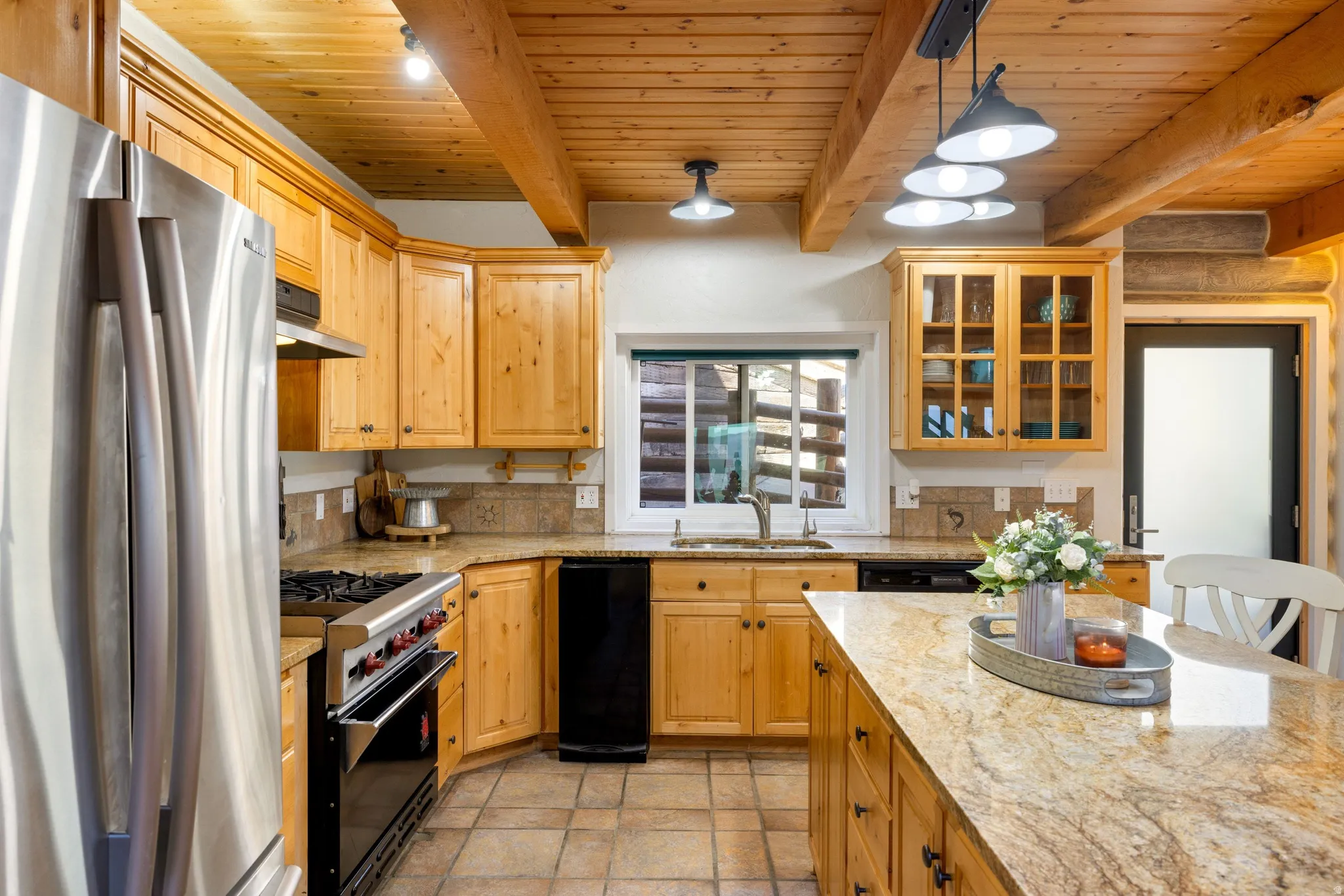 Kitchen with stainless steel appliances, light stone countertops, a wood ceiling with exposed beams, decorative light fixtures, and glass fronted cabinets