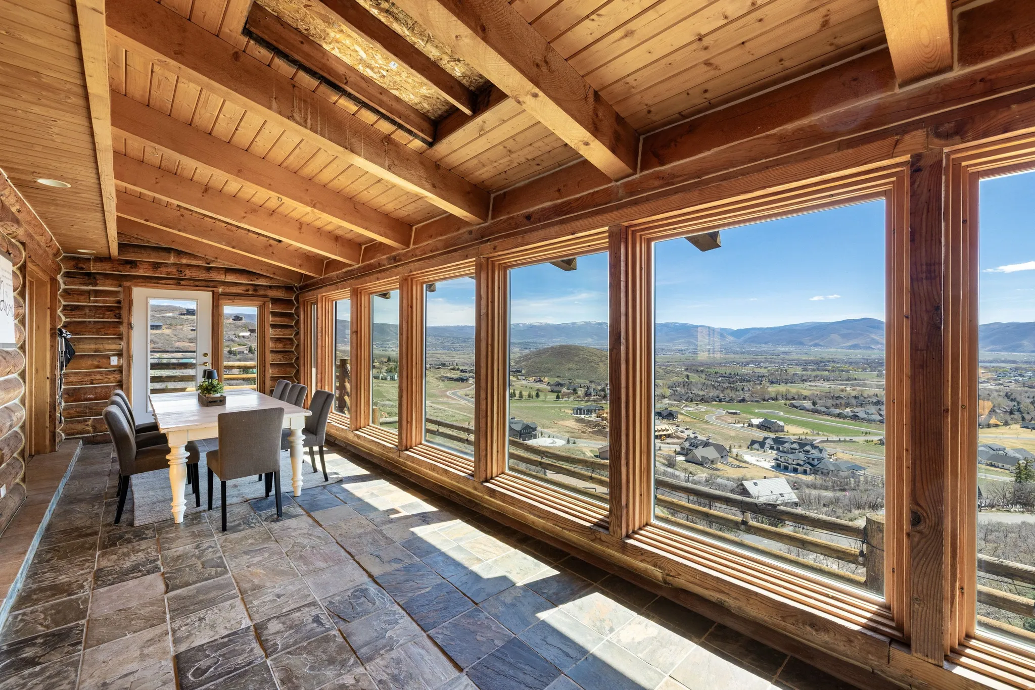 Sunroom featuring a mountain view, stone tile flooring, wooden ceiling, log walls, and lofted ceiling with beams