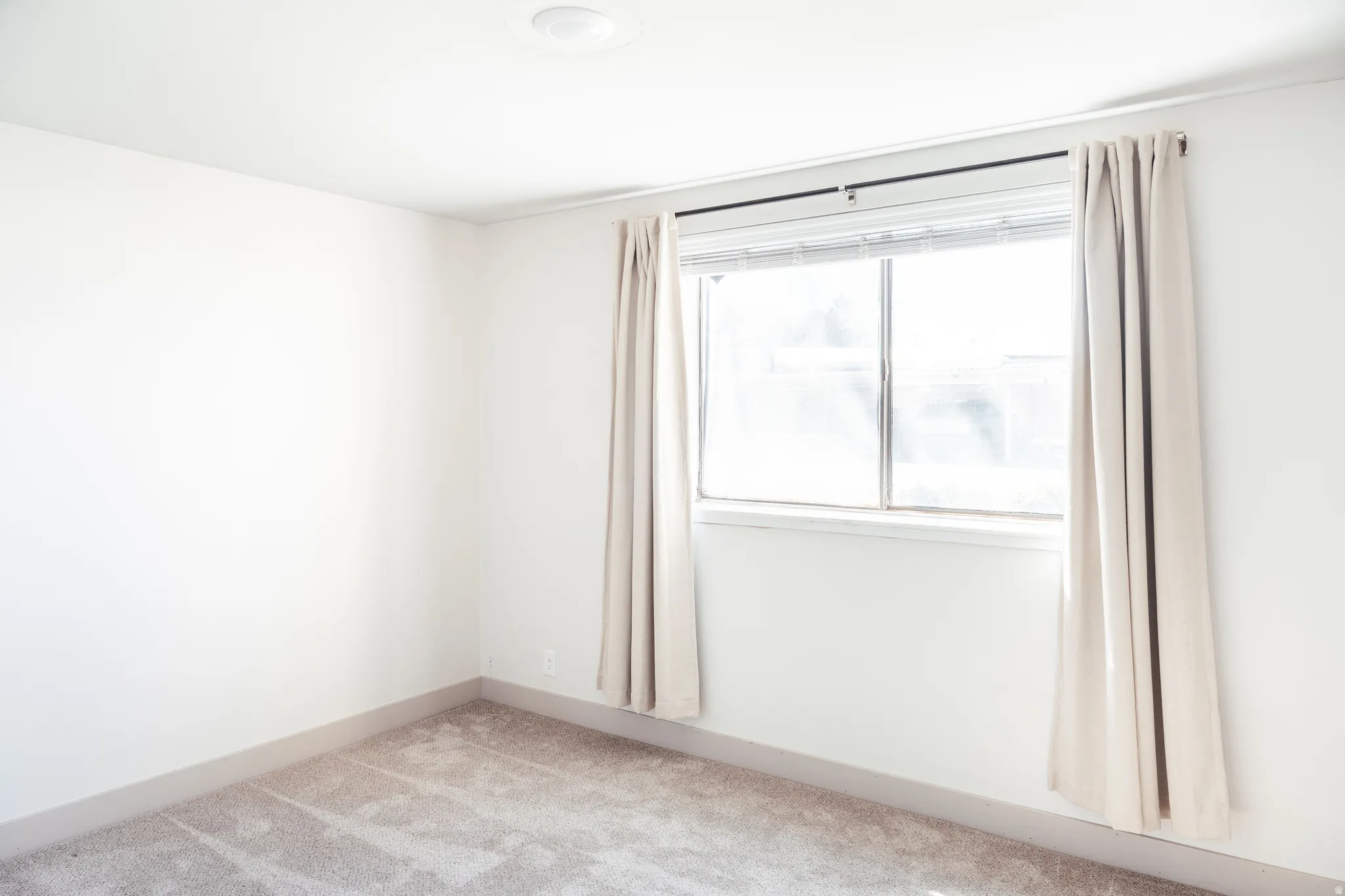 Empty room with light colored carpet and baseboards