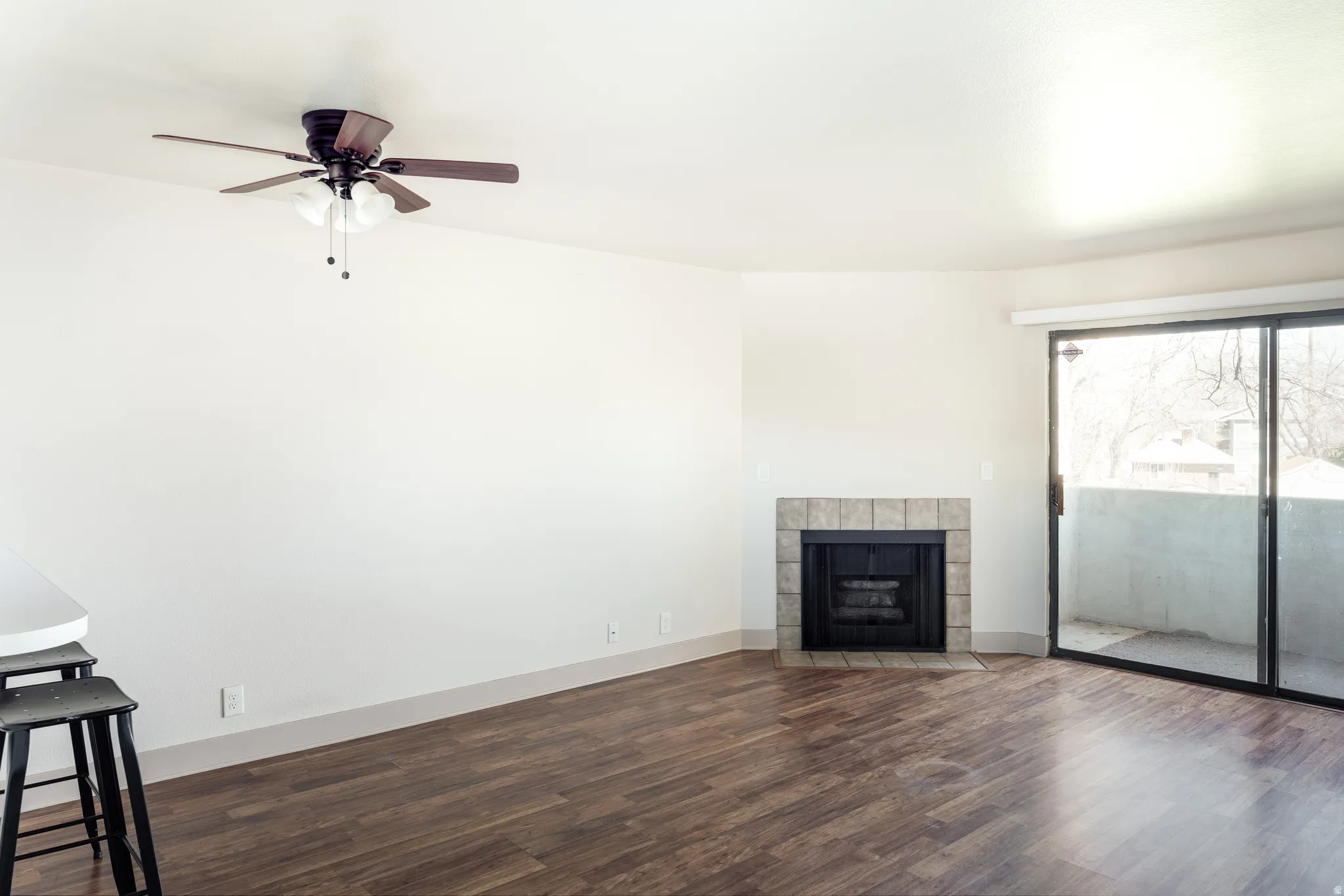 Unfurnished living room with dark wood-style flooring, a tile fireplace, and ceiling fan
