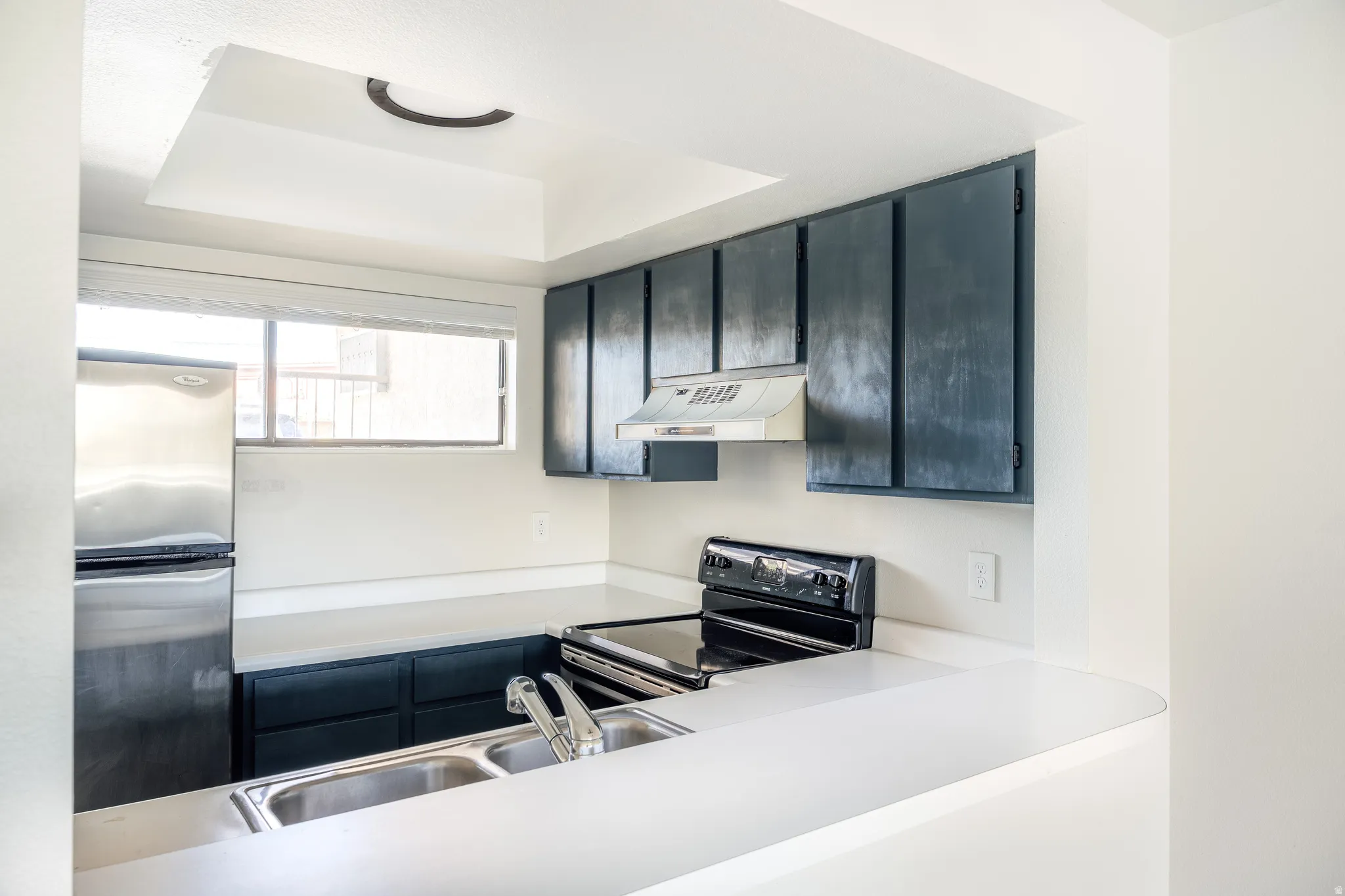 Kitchen featuring freestanding refrigerator, range with electric stovetop, light countertops, a tray ceiling, and dark cabinetry
