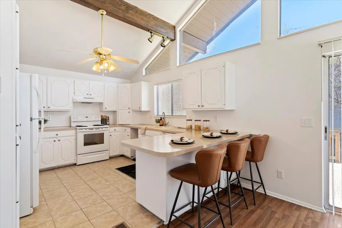 Kitchen featuring a breakfast bar, a peninsula, white cabinetry, white appliances, and light countertops