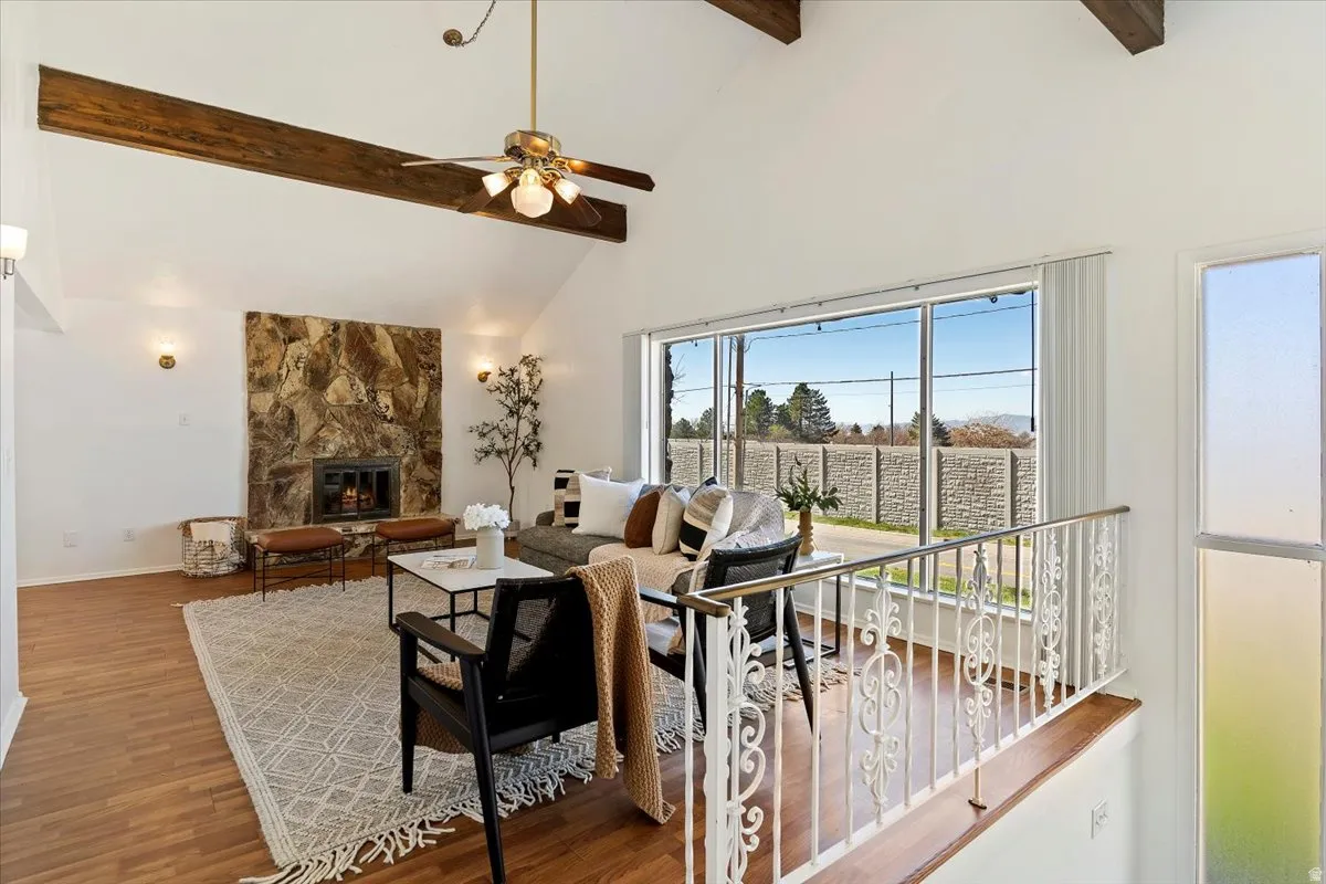 Living area with a stone fireplace, lofted ceiling, wood finished floors, and ceiling fan