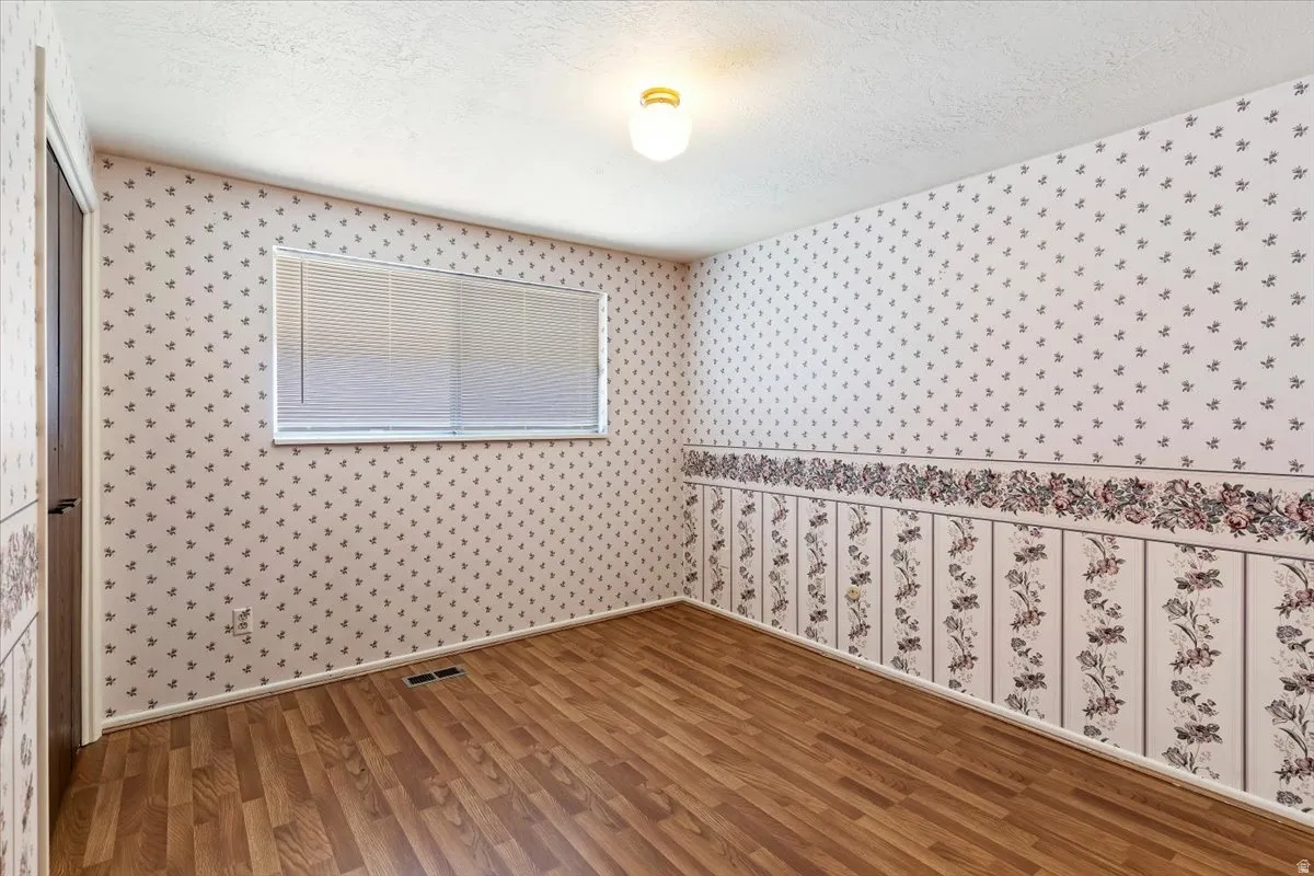 Spare room with wood finished floors, a textured ceiling, and wallpapered walls