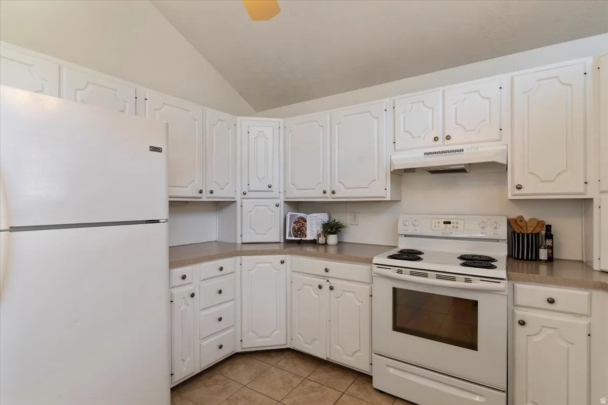 Kitchen featuring white appliances, white cabinetry, lofted ceiling, and light tile patterned floors