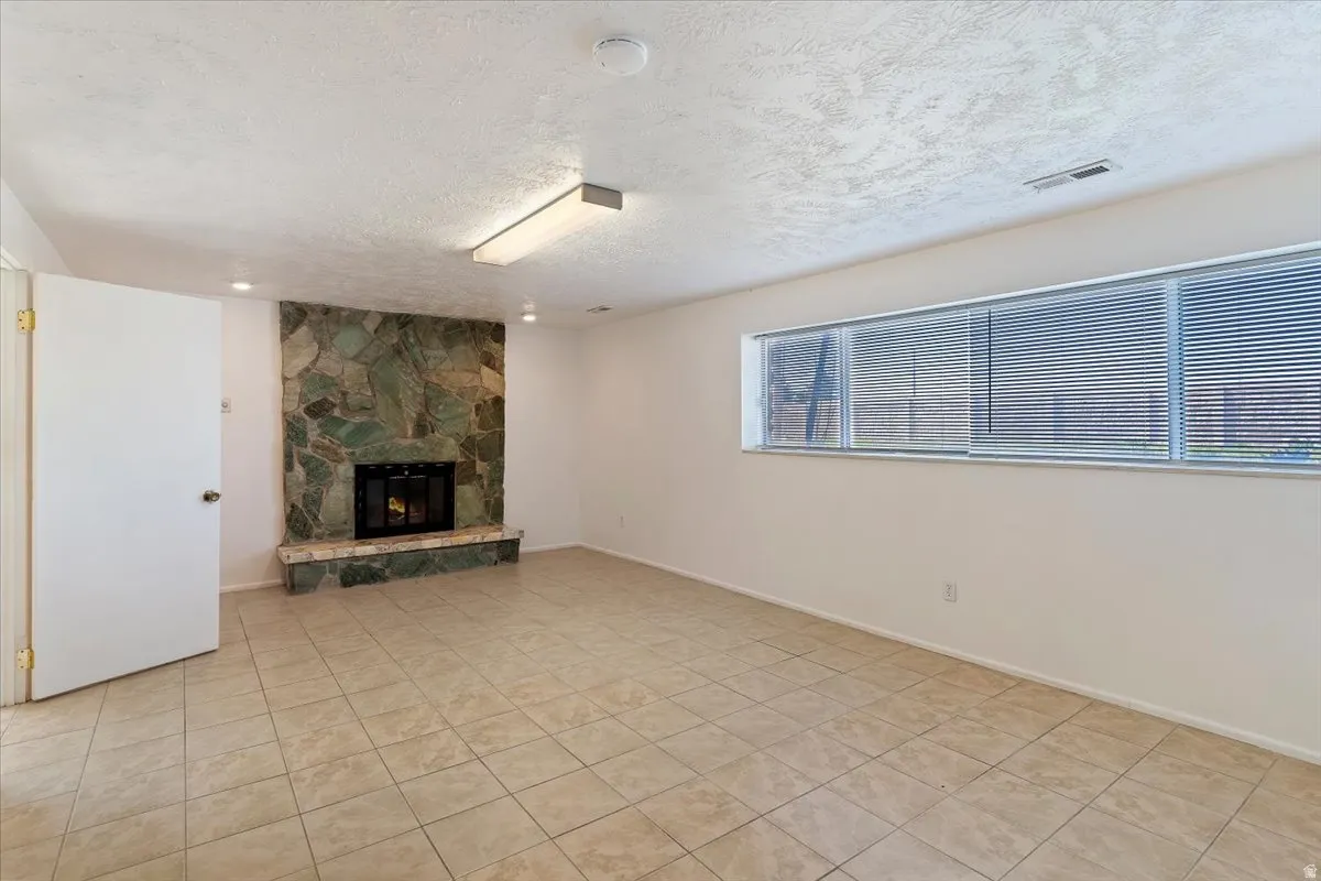 Unfurnished living room featuring a textured ceiling, a fireplace, and light tile patterned flooring