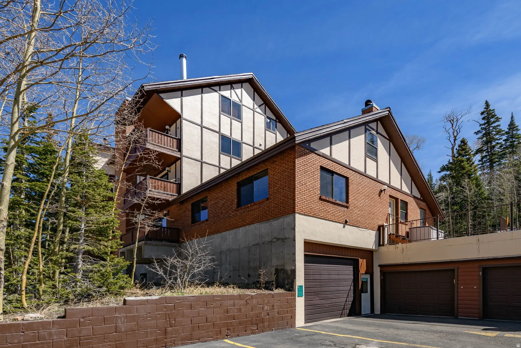 View of property exterior featuring brick siding, a balcony, an attached garage, and a chimney