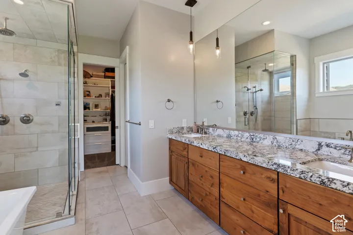 Full bathroom featuring a stall shower, double vanity, a soaking tub, a walk in closet, and light tile patterned flooring