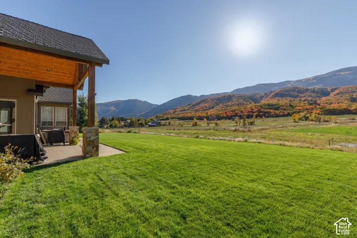 Expansive green lawn with a covered patio featuring wood-finish ceiling and stone-clad columns