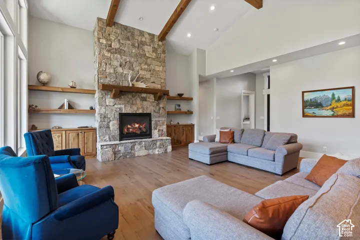 Living room featuring light wood floors, a stone fireplace, and vaulted ceiling with custom beams.