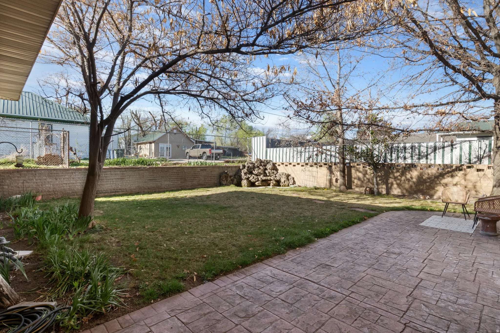 Fenced backyard with stamped concrete patio and water feature in the corner with goldfish.