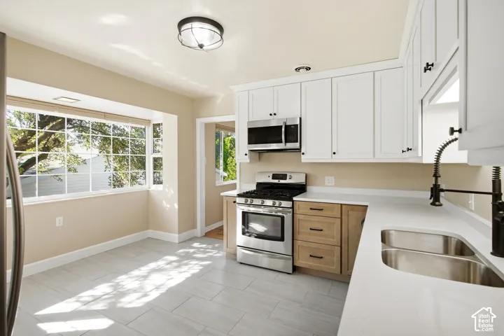 Kitchen featuring shaker-style cabinetry, stainless steel appliances, a dual basin sink with a gooseneck faucet, light-toned countertops, and a bay window