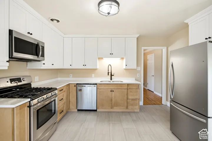 Kitchen featuring stainless steel appliances, two-tone cabinetry, light-toned countertops, and a modern ceiling light fixture