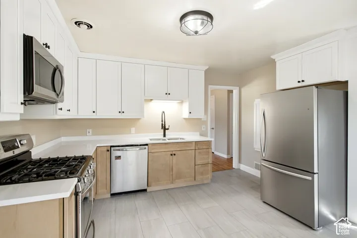 Kitchen featuring white upper cabinetry, wood-finish lower cabinetry, light-toned countertops, and stainless steel appliances