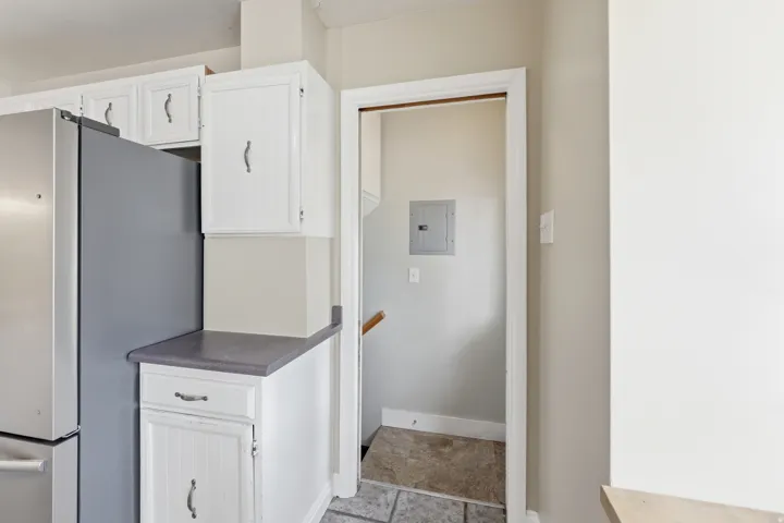 Kitchen with freestanding refrigerator, white cabinets, dark countertops, and electric panel