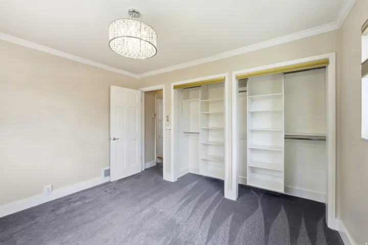 Unfurnished bedroom with two closets, dark colored carpet, ornamental molding, and hanging lights