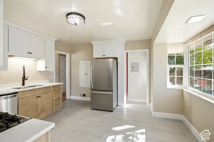 Bright kitchen featuring white upper cabinetry, wood-finish lower cabinetry, white countertops, and stainless steel appliances