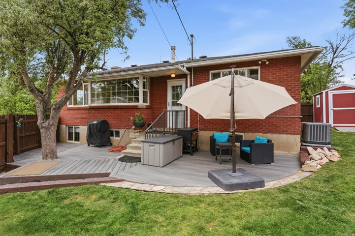 Rear view of house with a deck, brick siding, an outdoor living space, a storage unit, and a patio area