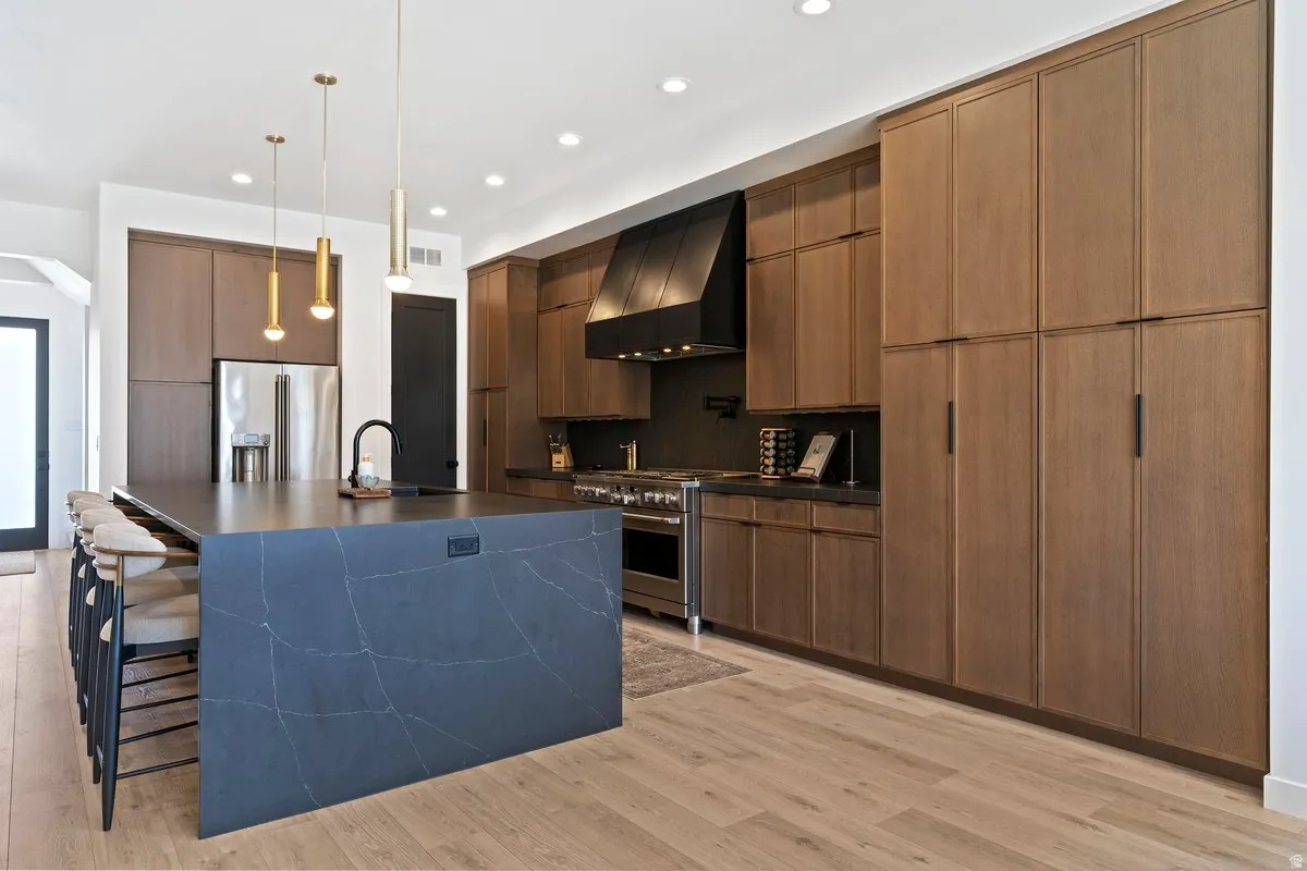 Kitchen featuring modern cabinets, premium appliances, decorative light fixtures, light wood-type flooring, and a large island