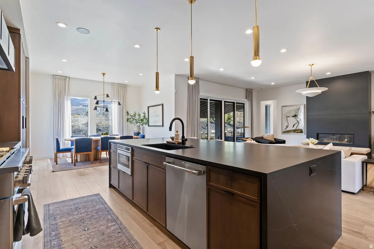 Kitchen with an island with sink, light wood-style floors, stainless steel appliances, dark wood finish cabinetry, and hanging light fixtures