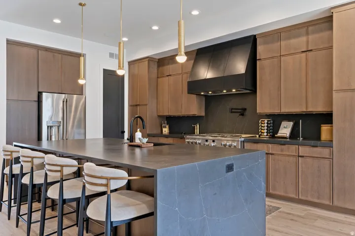 Kitchen featuring a breakfast bar area, a large island with sink, extractor fan, stainless steel appliances, and light wood finished floors