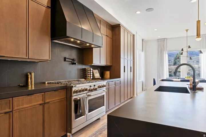 Kitchen featuring range with two ovens, hanging light fixtures, decorative backsplash, light wood-type flooring, and wood finish cabinets