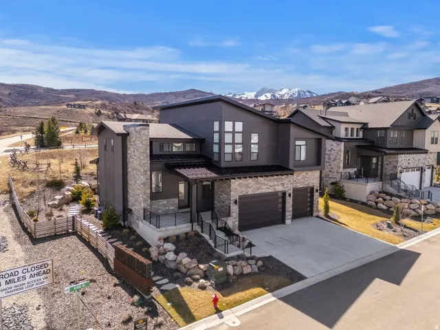 View of front of home with stone siding, an attached garage, a mountain view, concrete driveway, and covered porch