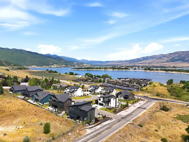 Modern residential development featuring a prominent waterside setting, paved roads, and distant mountain backdrops