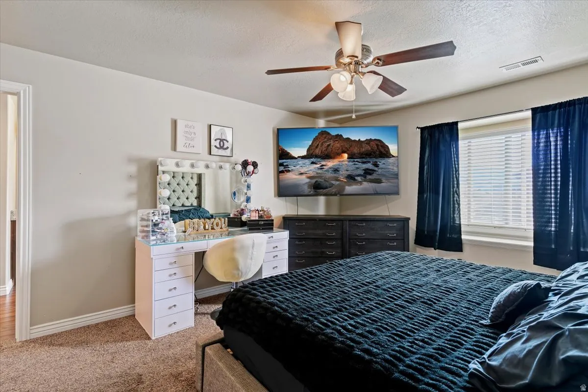 Bedroom with a textured ceiling, light colored carpet, and a ceiling fan