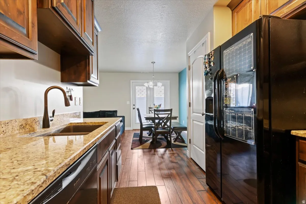 Kitchen with light stone counters, black appliances, a textured ceiling, dark wood-type flooring, and a chandelier