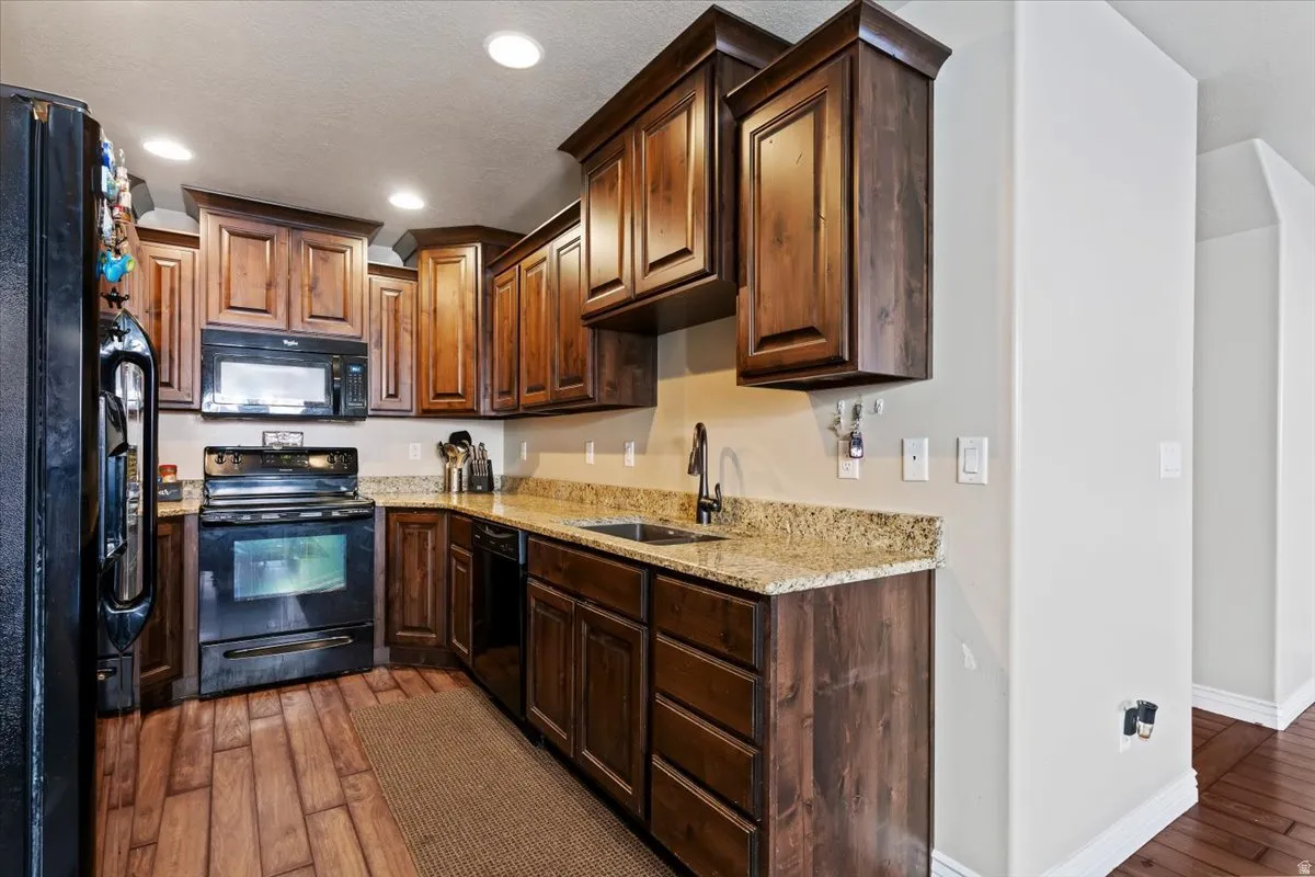 Kitchen with black appliances, light stone counters, light wood-style floors, dark wood finish cabinets, and recessed lighting