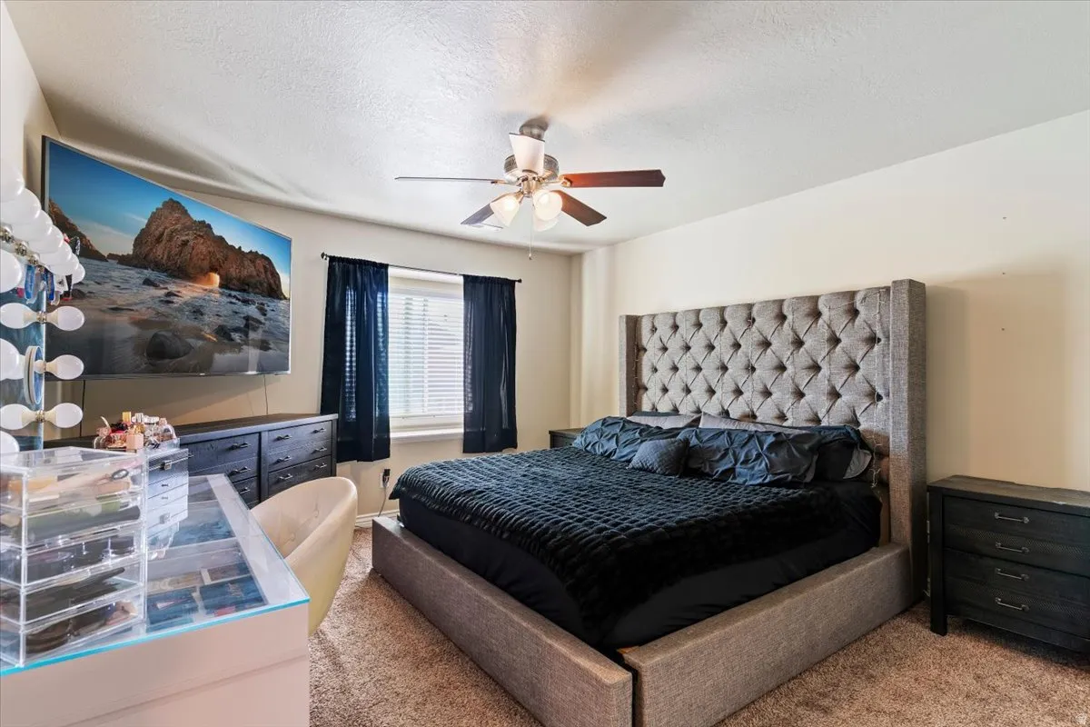 Carpeted bedroom with ceiling fan and a textured ceiling