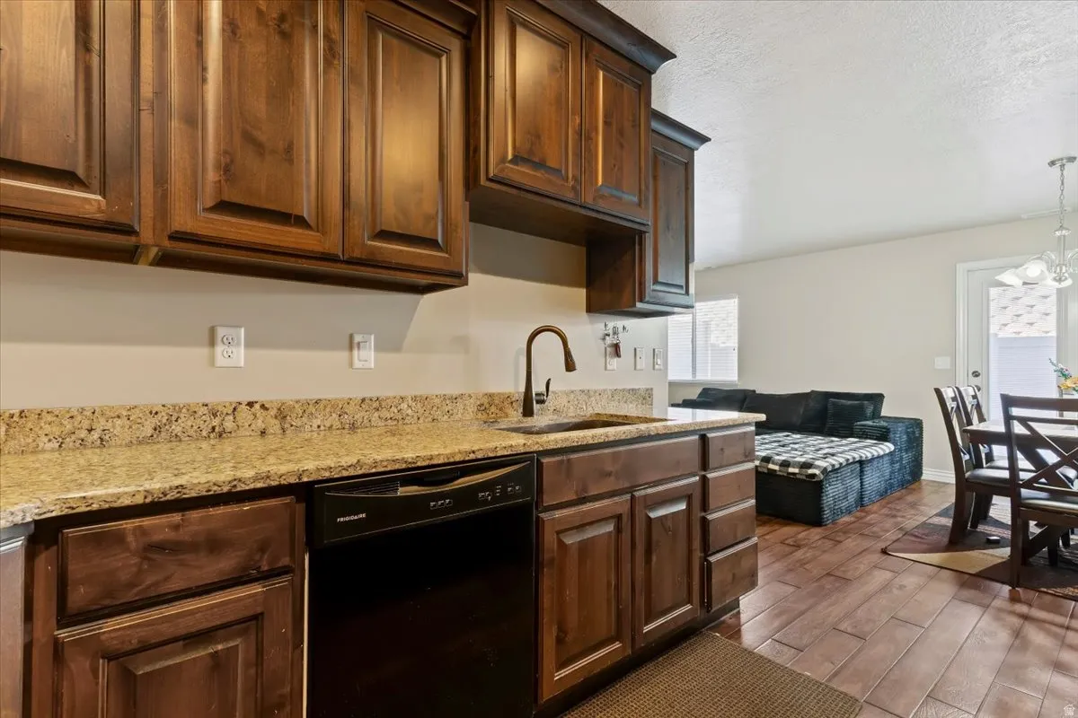 Kitchen with black dishwasher, dark wood-style floors, light stone countertops, a textured ceiling, and suspended lighting