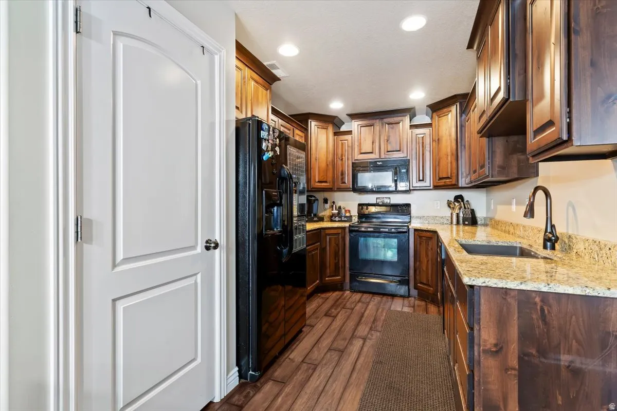 Kitchen with black appliances, light stone countertops, recessed lighting, and dark wood-style floors