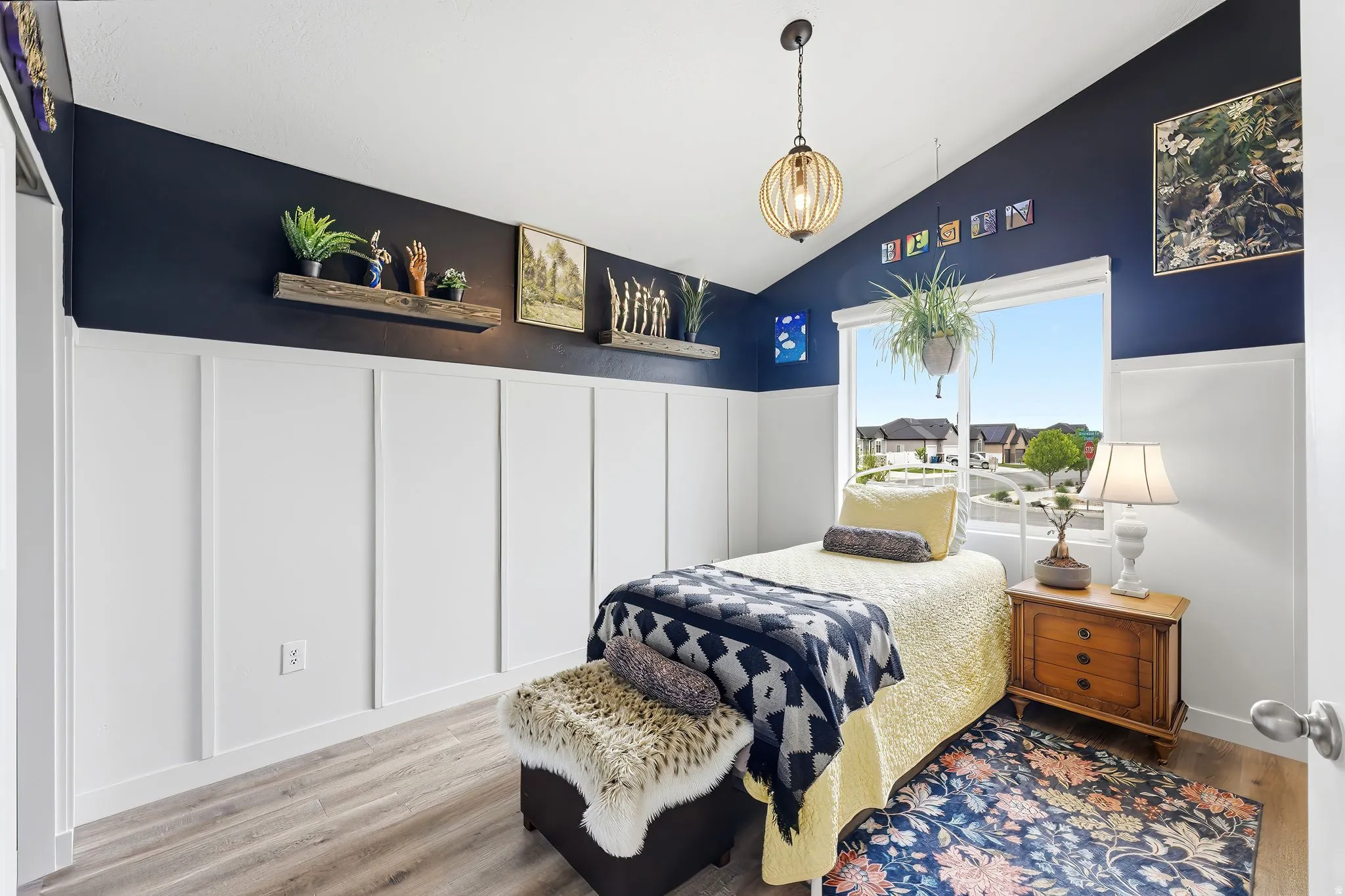 Bedroom featuring vaulted ceiling, wainscoting, wood finished floors, and a decorative wall