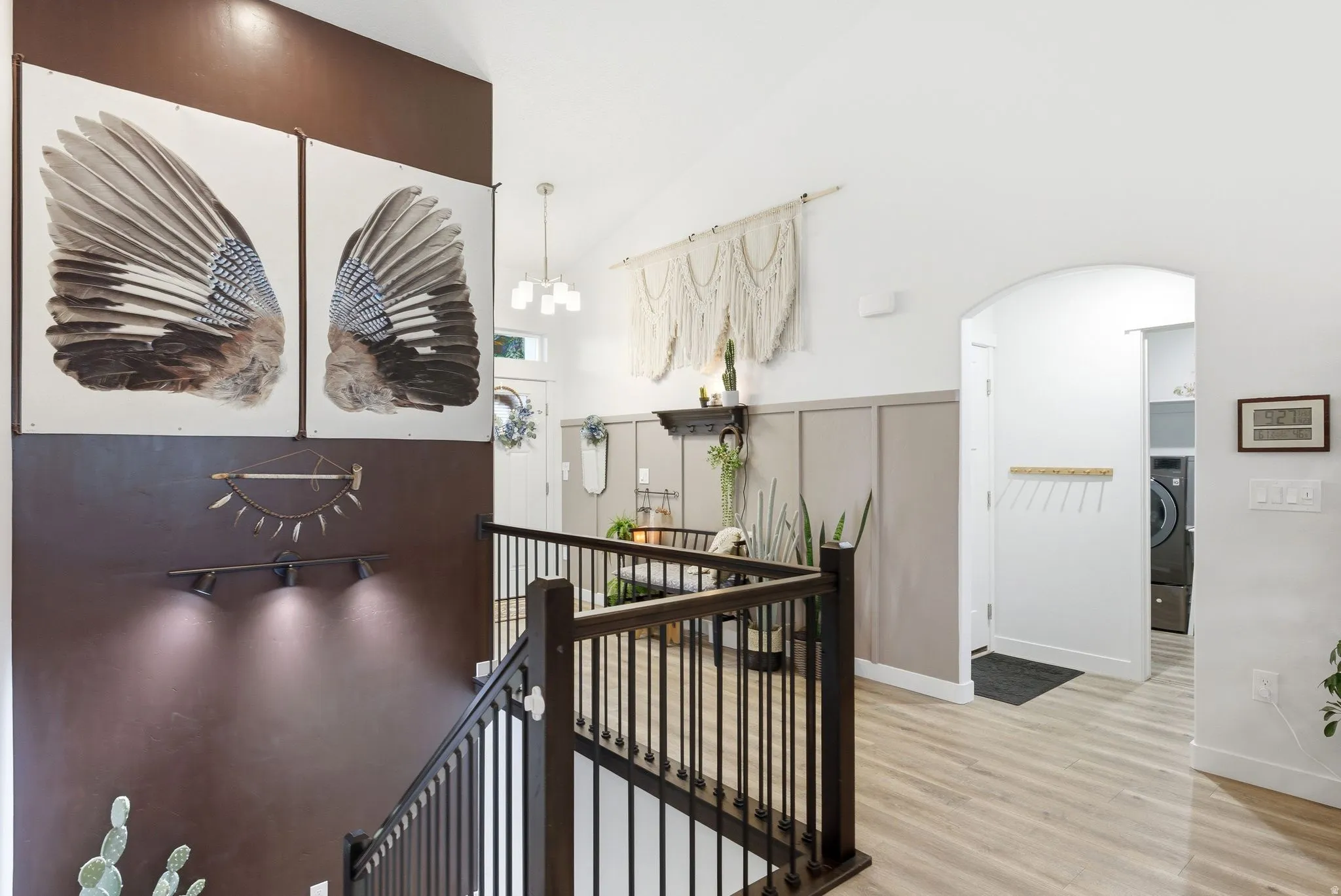 Corridor featuring arched walkways, light wood finished floors, an upstairs landing, lofted ceiling, and hanging lights