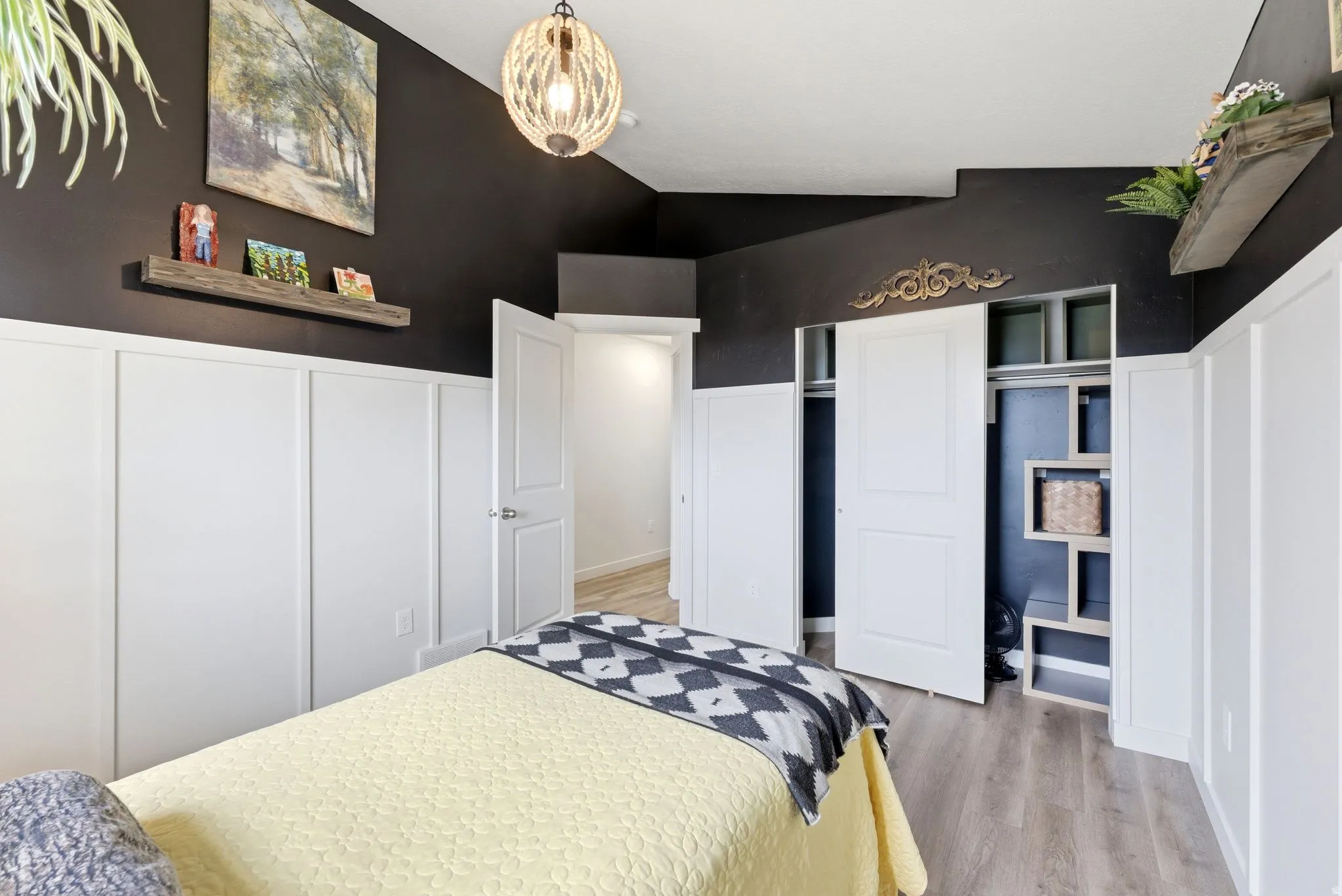 Bedroom featuring light wood finished floors, wainscoting, a decorative wall, a closet, and lofted ceiling