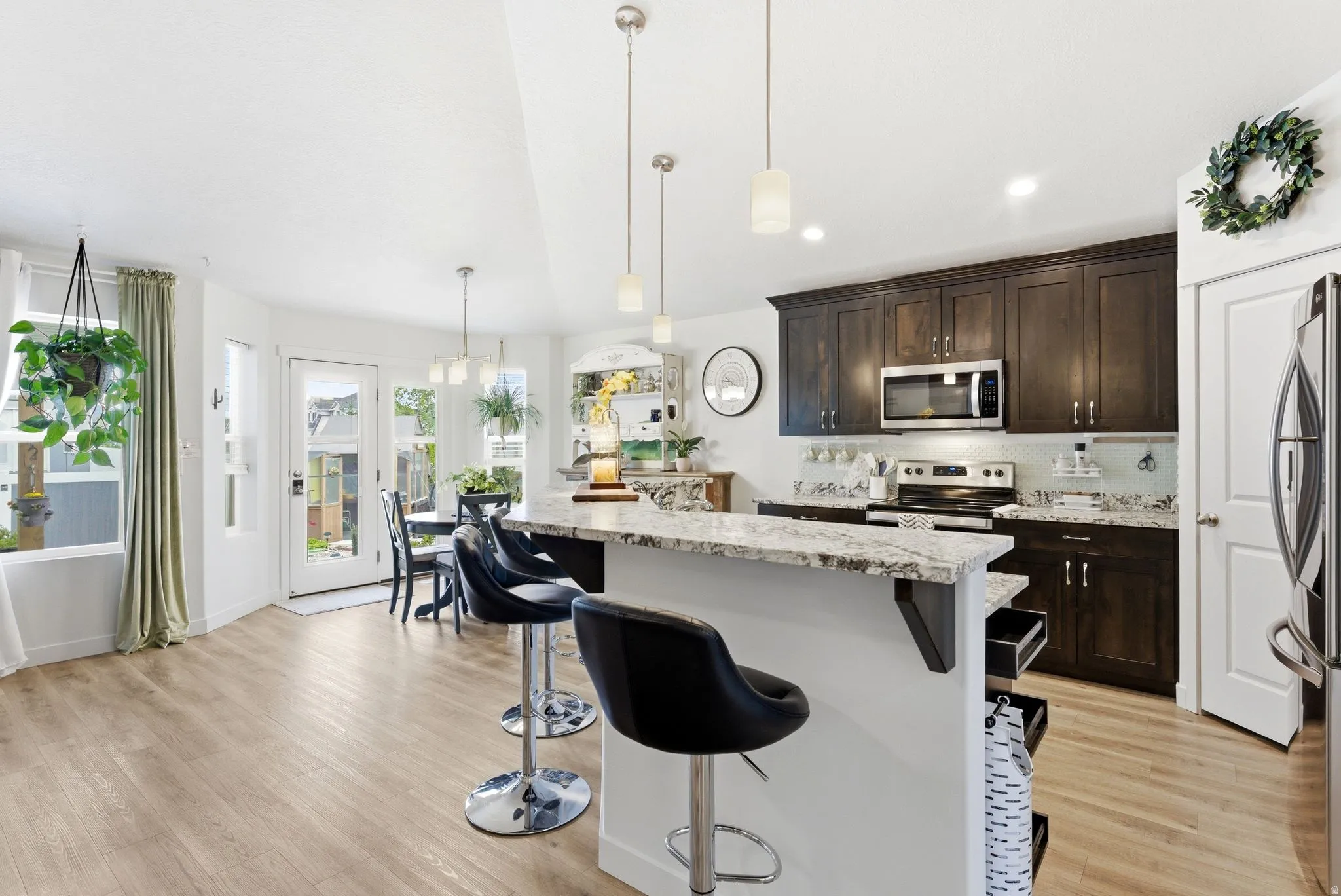 Kitchen with dark wood finish cabinetry, light wood-style flooring, pendant lighting, and a breakfast bar area